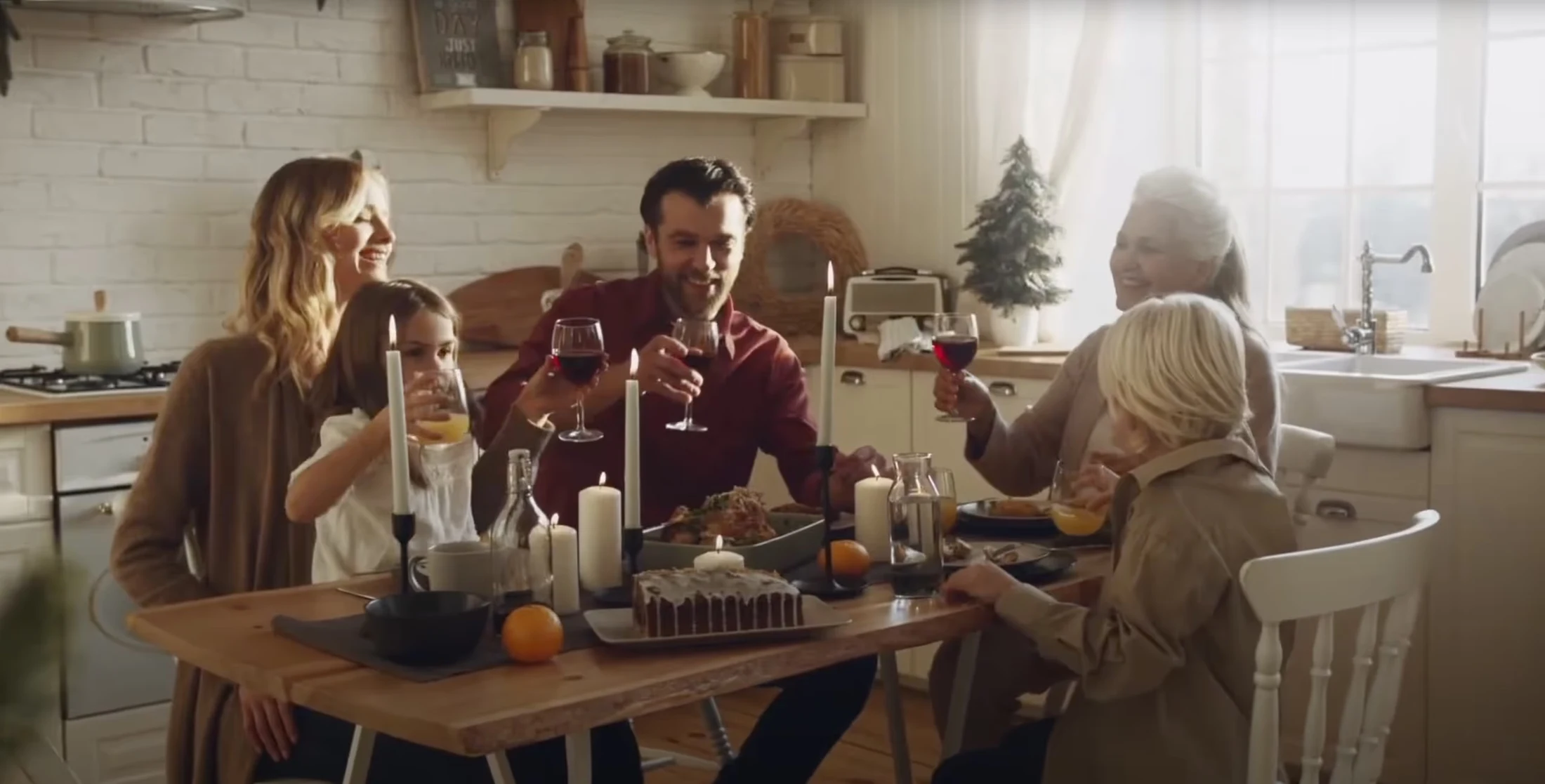 Familie bei einem festlichen Essen in einer gemütlichen, lichtdurchfluteten Küche, hebt Gläser zum Anstoßen.