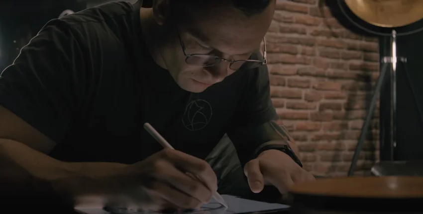 Künstler konzentriert beim Zeichnen auf einem Tablet, im Hintergrund eine rustikale Backsteinwand und Studiolicht.
