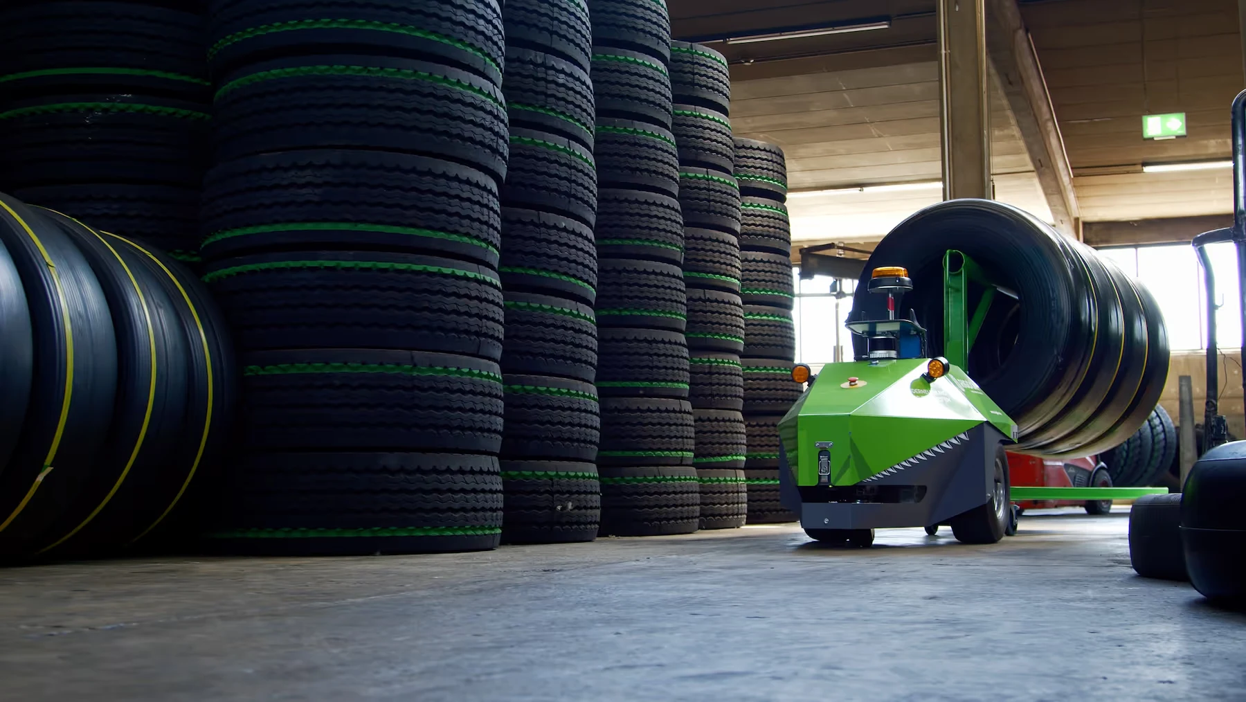Grüner autonomer Roboter transportiert große Reifen in einem Lager, symbolisiert innovative Logistiklösungen und Automatisierung.