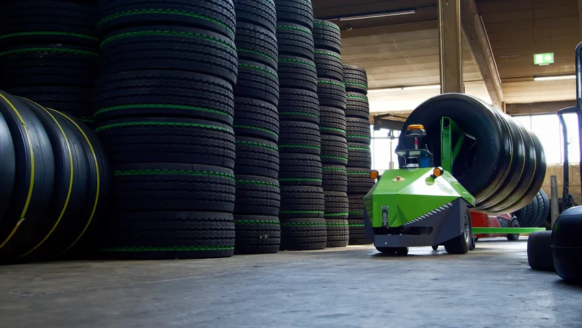 Grüner autonomer Roboter transportiert große Reifen in einem Lager, symbolisiert innovative Logistiklösungen und Automatisierung.