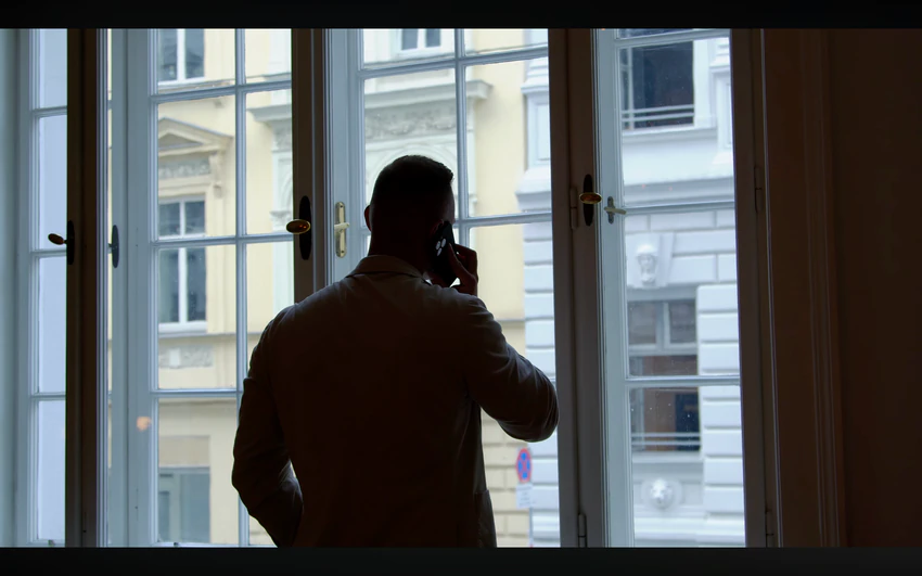 Ein Mann telefoniert vor einer großen Fensterfront, Filmstill aus dem Imagefilm der lumisol GmbH.